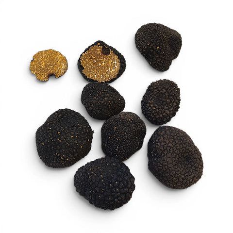 Sept truffes noires, dont deux moitiés montrant leur intérieur brun doré, disposées sur un fond blanc uni.